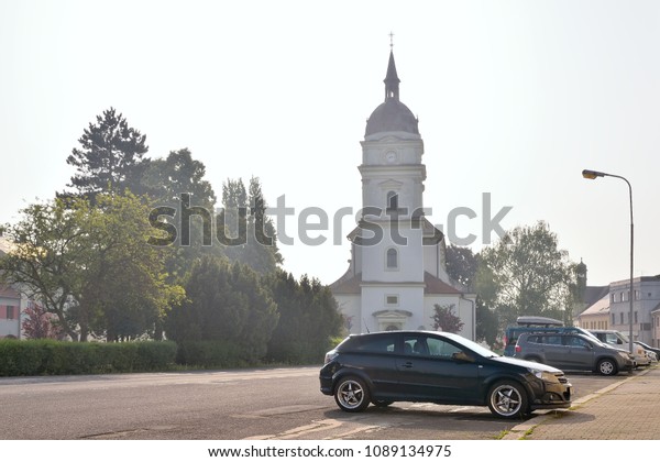 Chabarovice,\
Czech republic - May 12, 2018: cars, trees and Narozeni Panny Marie\
church on Husovo square at spring\
moning
