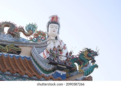 CHACHOENGSAO, THAILAND – DECEMBER 12, 2021: A statue of the Lady Buddha or Guan Im standing behind the roof of a Chinese shrine and the sky on the background on evening at Wat Saman Rattanaram temple.