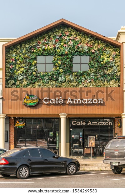 Chachoengsao, Thailand -\
March 17, 2019: Brown facade with green foliage and flowers labeled\
Café Amazon, a coffee house along Motorway 7. Cars parked up front.\
Light blue sky.