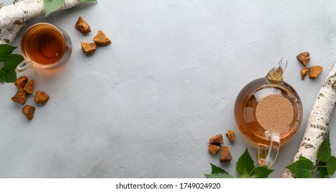 Chaga mushroom drink in a glass cup and teapot. Trendy healthy birch mushrooms. Top view with space for text, banner. Light gray stone background.