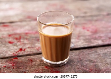 Chai, a hot Indian tea, served in a glass cup. An old wooden table sprinkled with red powder for the holy season of Indian New Year celebrations in the background. - Powered by Shutterstock