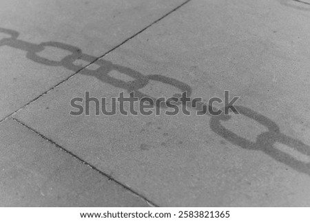 A chain casts a long shadow on a concrete surface, creating a striking black and white effect. The sunlight highlights the texture, evoking a sense of history and strength.