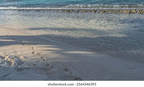 A chain of footprints of a man's bare feet runs on the sandy beach along the edge of clear turquoise water. Volcanic rocks are visible in the ocean. Mauritius. - Powered by Shutterstock