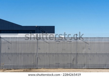 Chain link security fencing with vinyl slats and barbed wire topper in front of a building