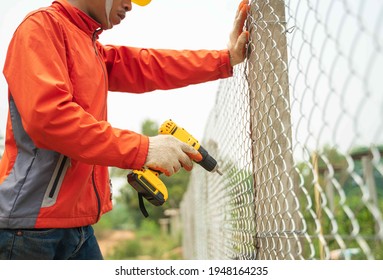 Chain link wire fences enclose border area Wire fence Metal net Wire mesh, Metal grater grille. Construction worker wear helmet and glove install wire mesh fence with screws drill cordless batterie.
				
				