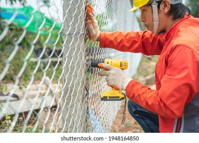 Chain link wire fences enclose border area Wire fence, Metal net Wire mesh Metal grater grille. Construction worker wear helmet and glove install wire mesh fence with screws drill cordless batterie.  