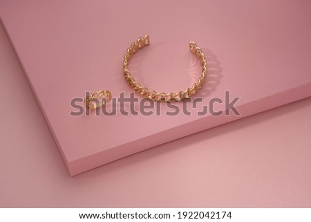 Chain shape golden bracelet and ring on pink background