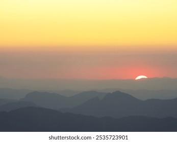 A chain of silhouetted mountains and in the background a breathtaking image of a red sun surrounded by black clouds in an orange sky. - Powered by Shutterstock