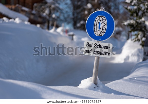 Chain traffic sign:\
Bei Schnee und Eisglätte. Blue warning information:  Snow chain\
obligation, Winter time and winter services. Snow covered road,\
trees. Styria, Austria