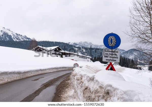 Chain traffic sign:\
Bei Schnee und Eisglätte. Blue warning information:  Snow chain\
obligation, Winter time and winter services. Snow covered road,\
trees. Styria, Austria