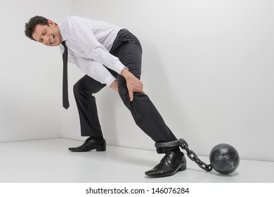 Chained businessman. Full length of hopeless businessman trying to go with shackles chained to his legs