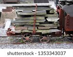 Chained stack of slate on cart with small metal wheels on rails slate held on by large chain at middle of load