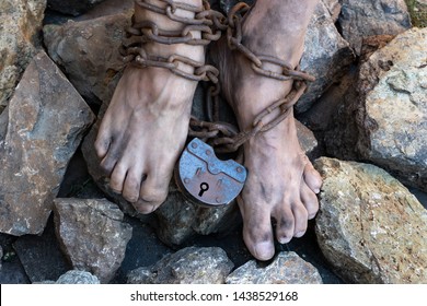 Chains with a lock on the legs of a slave amidst stones. Chains at the ankle. The symbol of slavery