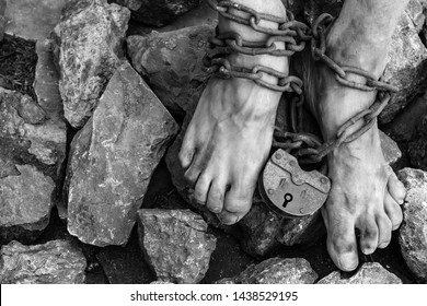 Chains with a lock on the legs of a slave amidst stones. Chains at the ankle. The symbol of slavery