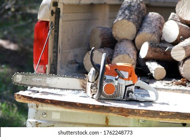 Chainsaw On Open Bed Of Beat Up Pickup Truck With Cut Logs In Background