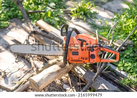 Chainsaw that stands on a heap of firewood in the yard on a beautiful background of green grass and forest.