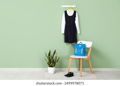 Chair with backpack, houseplant and stylish school uniform hanging on color wall in room - Powered by Shutterstock