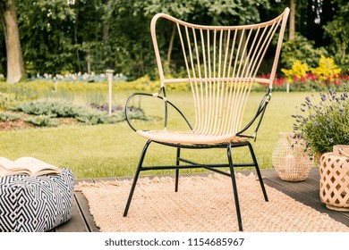 Chair On Rug On Patio With Flowers And Pouf In The Garden During Spring. Real Photo