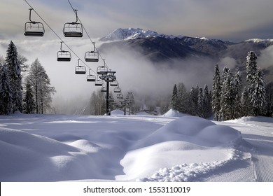 Chair ski lift in Krasnaya Polyana, Sochi, Russia on Chugush mountain peak background in Caucasus Mountains at snowy winter. Ski tracks of Gazprom ski resort on sunny day. Scenic landscape