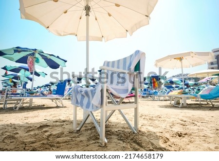 Chair with striped towel under an umbrella le at the beach on a sunny summer day. In the background, the beach equipped with sun loungers and umbrellas along the Adriatic Sea in Italy.
