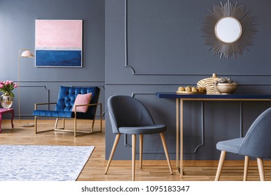 Chair at table in modern grey apartment interior with navy blue armchair, painting and mirror
