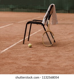 chair with towel and tennis racket with tennis ball at court