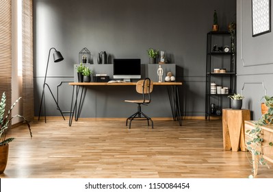 Chair at wooden table with computer monitor and plants in grey spacious home office interior