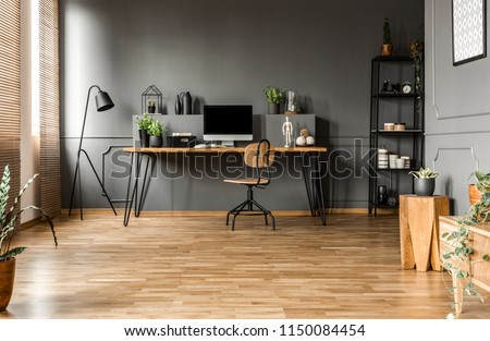 Chair at wooden table with computer monitor and plants in grey spacious home office interior