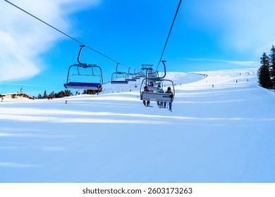 A chairlift carries enthusiastic skiers and snowboarders over a beautiful snow-covered mountain landscape. The bright sun shines on this perfect winter day, inviting outdoor adventures.