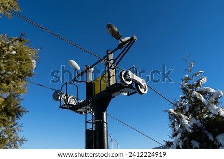 Chairlift intermediate supporting tower with sheave. Stanchion and pulley mechanism, wheels with groove holding steel rope or cable on ski station chairlifts post.
