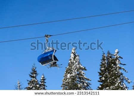 Chairlift of ropeway against blue sky. Cable car transports winter ski and snowboard riders. Ropeway. Germany, Black forest, Feldberg.
