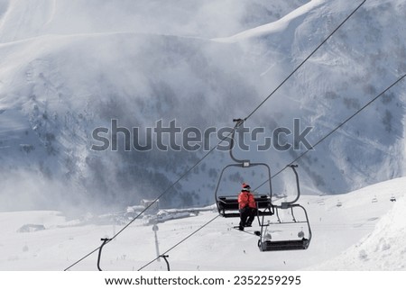 Chairlift with snowboarder in fog on ski resort at cold winter day. Snowy Caucasus Mountains. Georgia, region Gudauri.