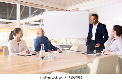 Chairman Of A Company Taking A Seat On The End Of The Conference Table In The Board Room, About To Start Going Through The Agenda With His Three Other Boarm Members.