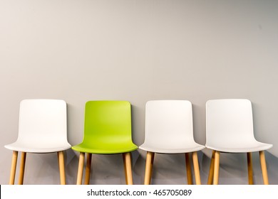 Chairs in modern design arranged in front of the gradient grey wall for interior or graphic backgrounds. The chair in different color can be used as a metaphor to represent the hiring position.