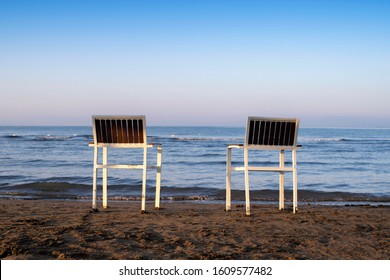 Chairs stand in the sand.Two empty chairs stand on beach in evening with view on marine sunset.