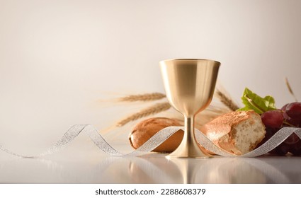 Chalice reflected on white table with bread and grapes behind with white isolated background. Front view.