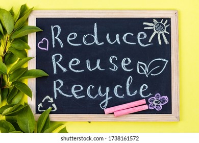 Chalk board Reduse Reuse Recycle sign on a yellow background with green leaves and chalk pieces. Top view