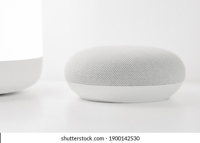 Chalk colored smart home voice assistant with a white backdrop. Smart home lamp at its side.