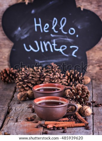 Chalk inscription "hello winter". Coffee, fir branch, nuts, cones, cozy knitted blanket. Winter, New Year, Christmas still life.