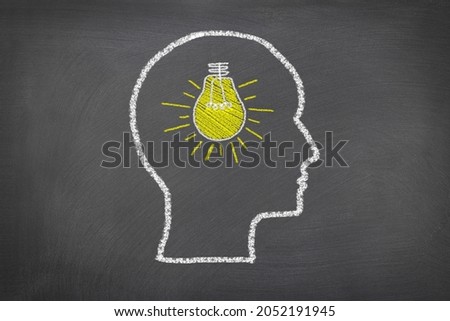 A chalk sketch on a blackboard of a human head and lightbulb that represents thoughts and ideas, for use as any science theme or consideration of how humans think.

