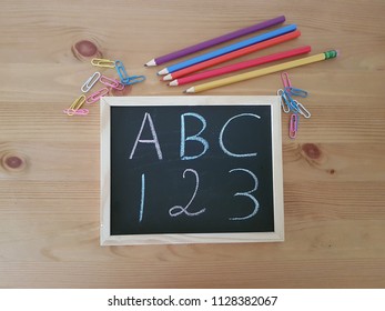 Chalkboard with ABC, 123 and colored pencils laying on a wooden table, School supplies, Elementary school, Kindergarten, 