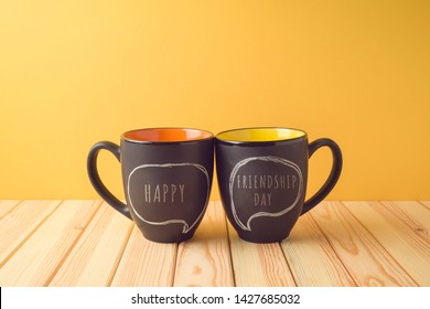 Chalkboard coffee mugs on wooden table with happy friendship day text. Friendship day concept - Shutterstock ID 1427685032