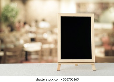 Chalkboard mockup, Blank chalk board menu standing on table over blur restaurant, Blackboard sign and blurred kitchen space for text, template, product display montage, backdrop, banner