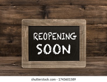 Chalkboard On Wooden Background. Reopening Soon Text