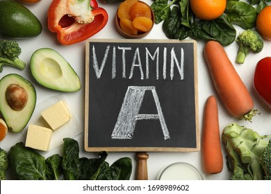 Chalkboard with phrase VITAMIN A and fresh products on white table, flat lay