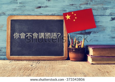 a chalkboard with the question do you speak chinese? written in chinese, a pot with pencils, some books and the flag of china, on a wooden desk