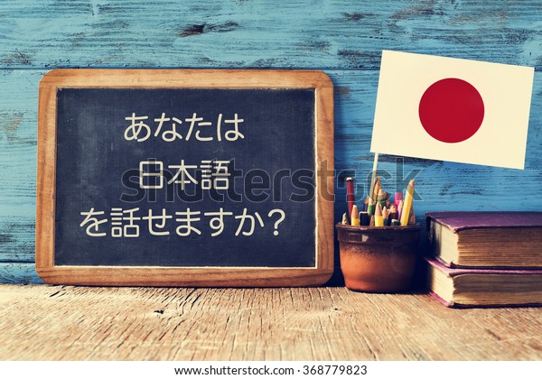 a chalkboard with the question do you speak\
Japanese? written in Japanese, a pot with pencils, some books and\
the flag of Japan, on a wooden\
desk