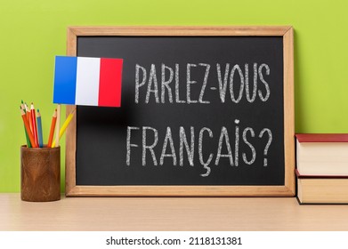 A chalkboard with the question parlez-vous francais? do you speak french? written in french, a pot with
pencils and the flag of France, on a wooden desk with green background