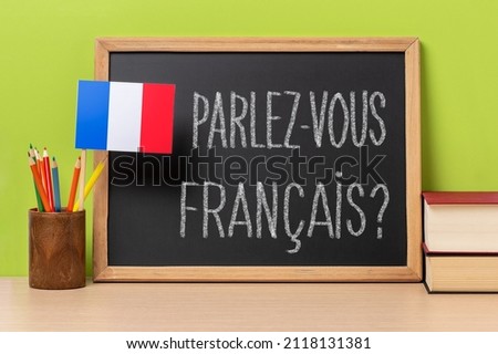 A chalkboard with the question parlez-vous francais? do you speak french? written in french, a pot with
pencils and the flag of France, on a wooden desk with green background
