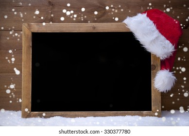 Chalkboard With Red Santa Hat On White Snow. Copy Space For Advertisement Or Christmas Greetings. Snowy Atmosphere With Snowflakes. Christmas Decoration With Brown Wooden Background - Powered by Shutterstock